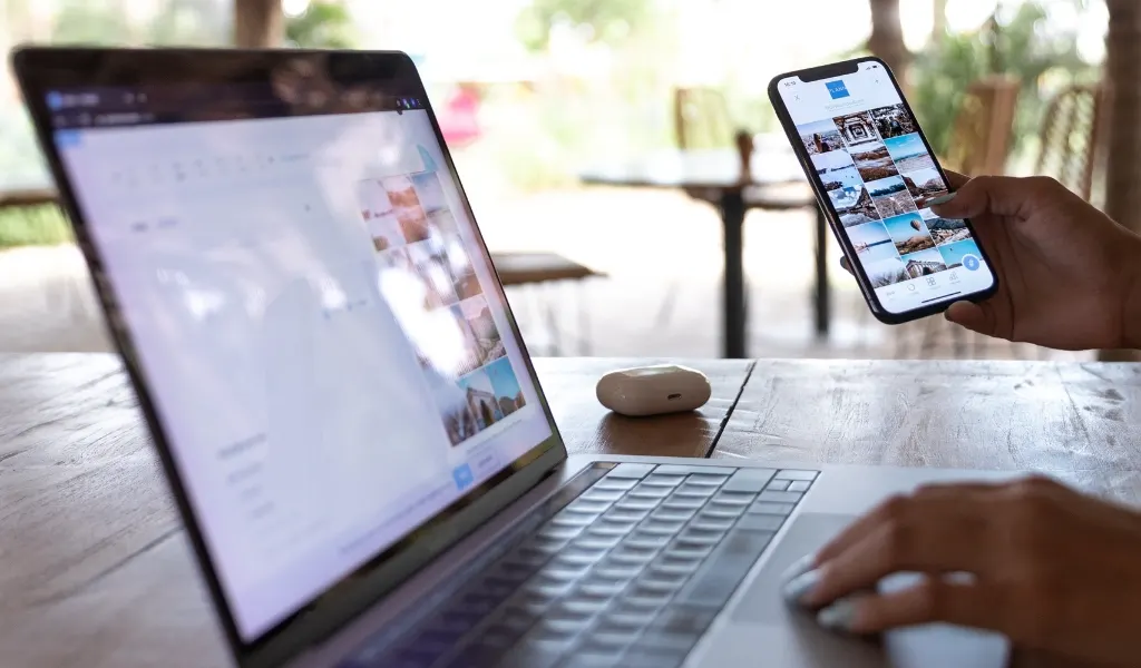 Bild på en öppen laptop och en person som håller i en telfon med ett instagram eller social media flöde uppe.