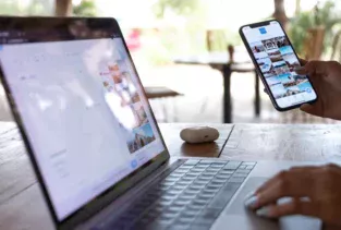 Bild på en öppen laptop och en person som håller i en telfon med ett instagram eller social media flöde uppe.
