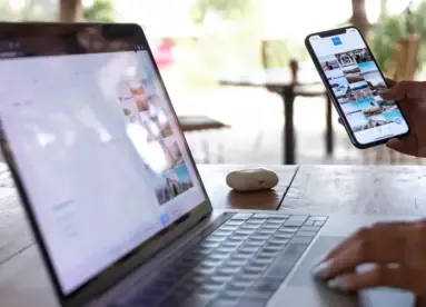Bild på en öppen laptop och en person som håller i en telfon med ett instagram eller social media flöde uppe.